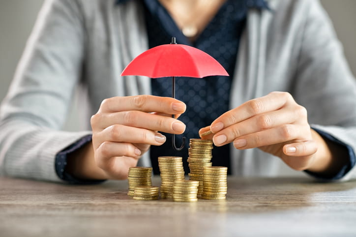 Hands protecting pile of coins with umbrella