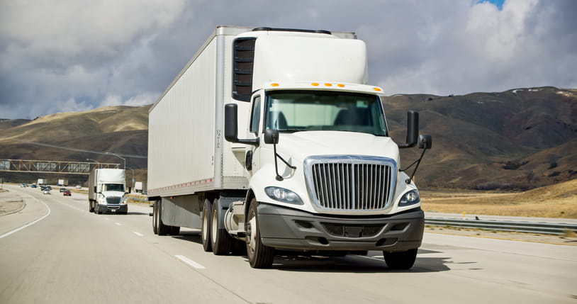 White semi-truck driving on highway with another truck in the background