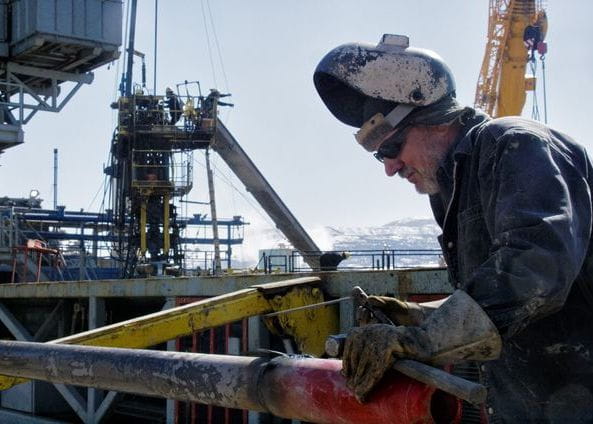 Worker welding on industrial platform with crane in background